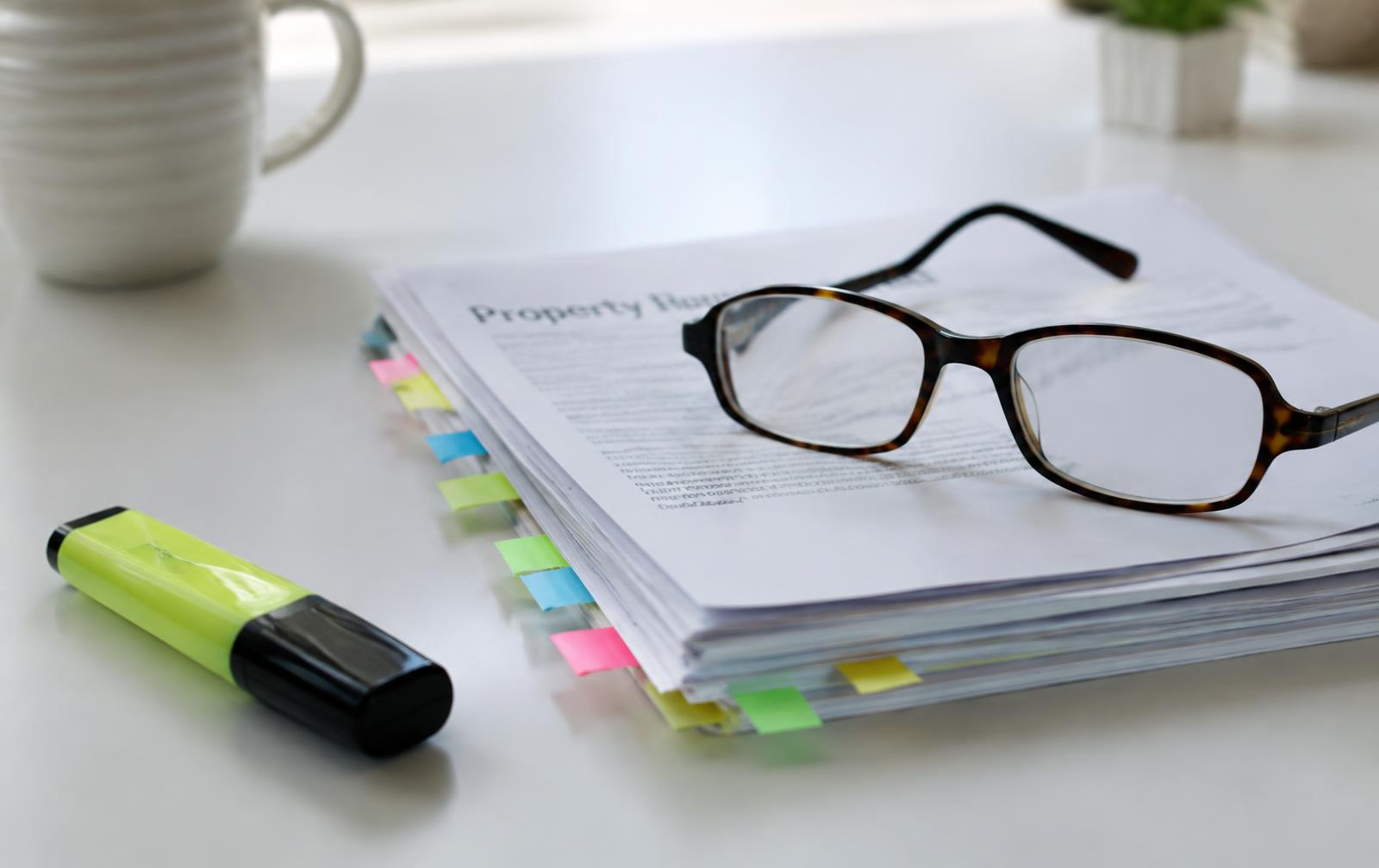 Tabbed stack of property documents with reading glasses and a highlighter